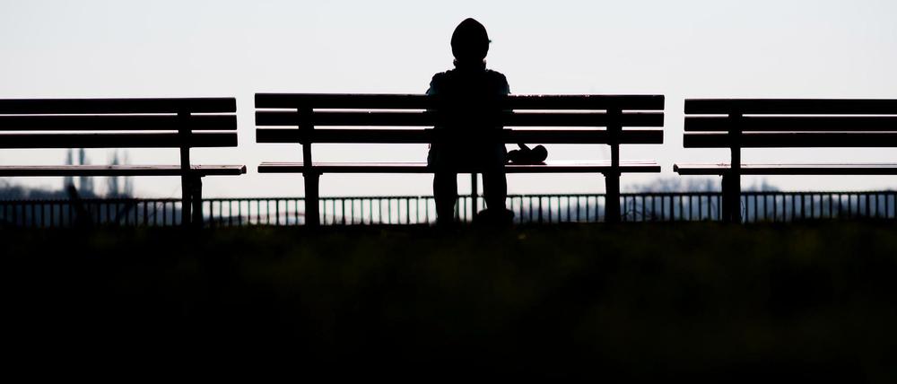 Eine Frau sitzt alleine auf einer Bank in der Sonne.