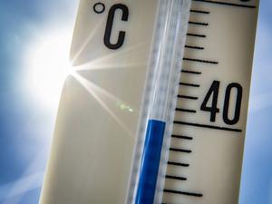 Ein Außenthermometer zeigt vor dem blauen Himmel und der Sonne eine Temperatur von nahezu 40 Grad Celsius an. 