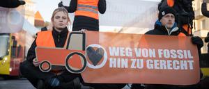 Aktivisten der Klimaschutzgruppe Letzte Generation sitzen bei einer Straßenblockade auf dem Innsbrucker Platz mit einem gemalten Traktor und einem Banner „Weg von fossil hin zu gerecht“ auf der Straße.