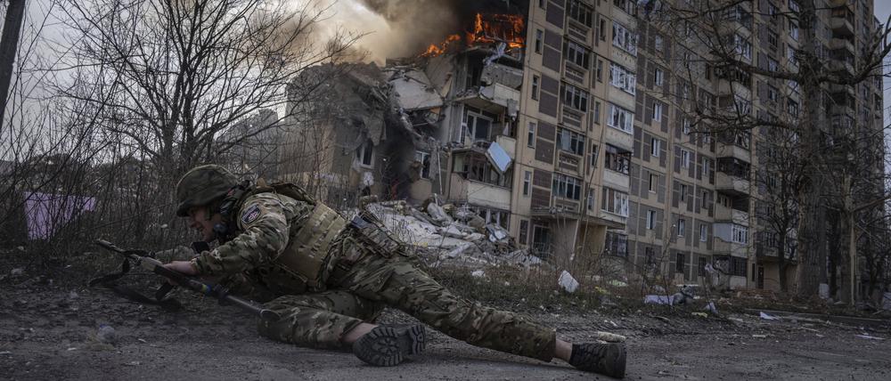 17.03.2023, Ukraine, Awdijiwka: Ein ukrainischer Polizist geht vor einem brennenden Gebäude in Deckung.