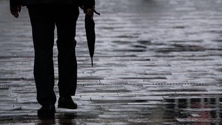 Ein Passant geht mit einem Regenschirm in der Hand durch eine Fußgängerzone.