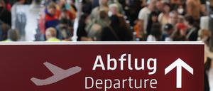 Am Flughafen Berlin-Brandenburg stehen zahlreiche Reisende in einer Schlange zur Sicherheitskontrolle hinter einem Schild mit der Aufschrift „Abflug“.