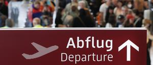  Am Flughafen Berlin Brandenburg BER stehen zahlreiche Reisende in einer Schlange zur Sicherheitskontrolle hinter einem Schild mit der Aufschrift „Abflug“. 