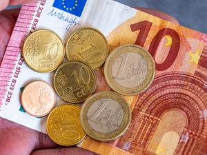 Geldscheine und Euro-Münzen mit dem Wert von 12,41 Euro liegen auf einer Hand – der derzeitige Mindestlohn in Deutschland.