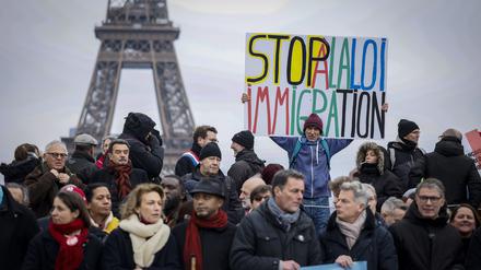 Ein Gegner des französischen Einwanderungsgesetzes hält während einer Demonstration ein Plakat mit der Aufschrift „Stoppt das Einwanderungsgesetz“ auf dem Trocadero-Platz in der Nähe des Eiffelturms.