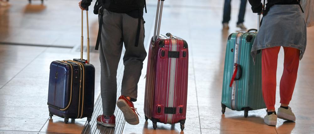 Reisende gehen im Flughafen Berlin-Brandenburg (BER) mit Koffern durch den Abflugsterminal.