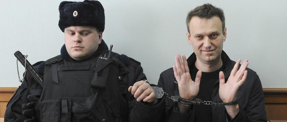 Der russische Oppositionsführer Alexej Nawalny (r) winkt für die Presse, während er in Handschellen vor Gericht sitzt. Der russische Oppositionspolitiker Alexej Nawalny ist nach Angaben der Justiz in Haft gestorben. Das teilte die Gefängnisverwaltung des nordrussischen Gebietes Jamal nach Angaben der Agentur Tass mit.