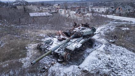 Ein zerstörter russischer Panzer, der von Schnee bedeckt ist, steht neben einer Straße.