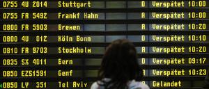 Eine Frau steht auf dem Flughafen Berlin-Schönefeld vor einer Anzeigetafel, auf der verspätete Flüge aufgelistet werden. 