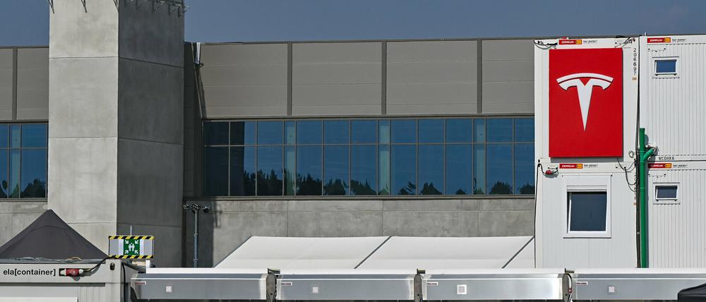 Das Logo der Firma Tesla an einem Baucontainer vor einer Halle der Autofabrik in Grünheide.