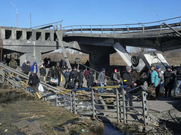 Ukrainer überqueren einen improvisierten Weg unter einer zerstörten Brücke auf der Flucht aus Irpin nordwestlich von Kiew.