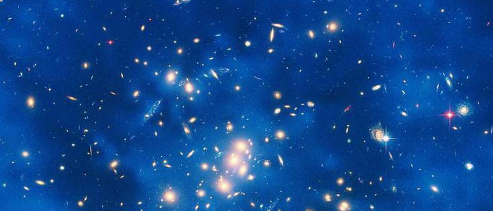 Was die Welt zusammenhält. Der Nachweis von schweren Gravitinos wäre ein wichtiger Schritt zur allenthalben gesuchten vereinheitlichten Theorie der Physik. Die Dunkle Materie, die aus diesen Teilchen bestehen könnte, macht sich nur über Gravitationseffekte bemerkbar. Die Aufnahme zeigt einen Ring Dunkler Materie in einem fünf Milliarden Lichtjahre entfernten Galaxienhaufen im Sternbild Fische. 