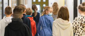In einer Gruppe von Schulkindern blickt ein Mädchen, dass einen medizinischen Mund-Nasen-Schutz trägt nach hinten.