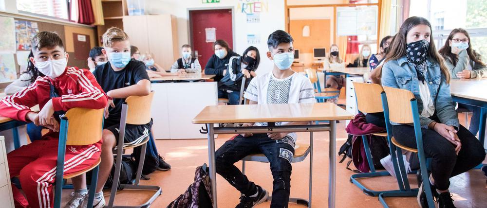 Siebtklässler sitzen in einem Klassenraum an ihren Tischen und tragen Mund-Nasen-Schhutz.